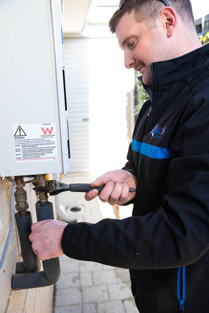 Ausco Plumbing & Gas team member working on outdoor hot water unit